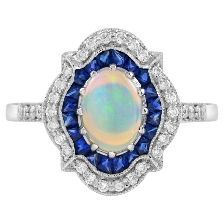 A totally unique opal, sapphire and diamond cluster ring of exceptional design. The center prong set with a magical natural opal displaying rainbow like hues. The opal is surrounded by a halo of French cut blue sapphires and sparkly diamonds in a cluster design. Crafted in solid 14k gold. The unusual combination of gemstones makes this ring a very special fine. Ring Information Style: Art-deco Metal: 14K White Gold Total weight: 3.73 g. (approx. total weight) Size: US7 (resizable) Center Gemstone Type: Opal Shape: Oval Cabochon Size: 8x6 mm. Number: 1 Weight: 0.80 Carat (approx.) Accent Gemstones I Type: Blue Sapphire Shape: French Cut Size: 1.8 - 2 mm. Number: 20 Weight: 0.95 Carat (approx.) Accent Gemstones II Type: Diamond Shape: Round Average Color: H Average Clarity: SI Size: 1.1 – 1. Unique Luxury Blue Opal Ring, Luxury Hallmarked Opal Ring With Oval Cabochon, Luxury Hallmarked Blue Opal Ring, Luxury Blue Multi-stone Opal Ring, Luxury Polished Opal Ring, Oval Cabochon, Cluster Design, Unique Opal, Rainbow Sapphires, Fine Ring