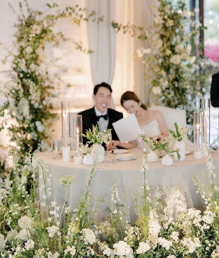 a bride and groom sitting at a table with flowers in front of them on their wedding day