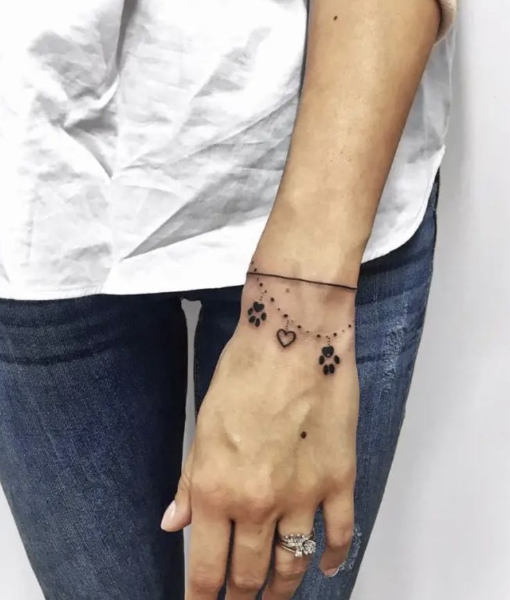 a woman's hand with a dog paw and heart tattoo on her left wrist