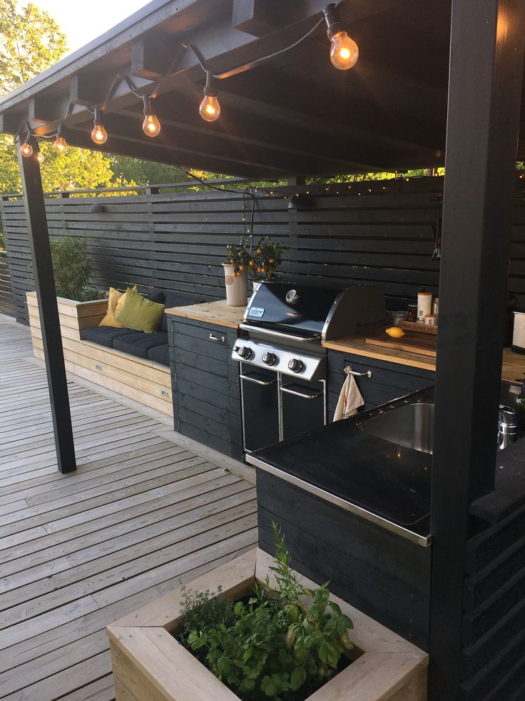 an outdoor kitchen with grill, sink and lights on the outside decking area next to it