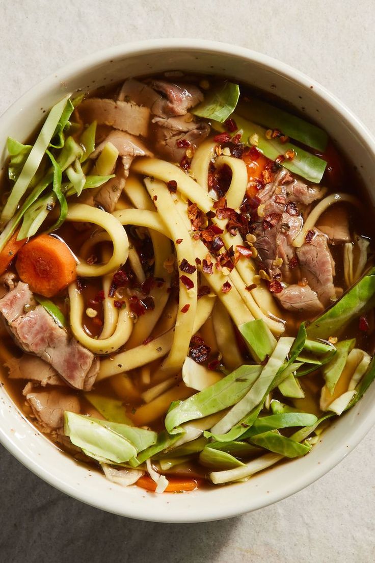 a bowl filled with noodles, meat and veggies on top of a table