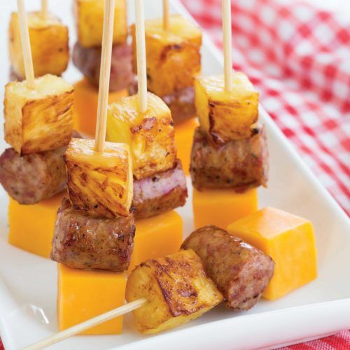 skewered meat and pineapples on a white plate with red checkered table cloth