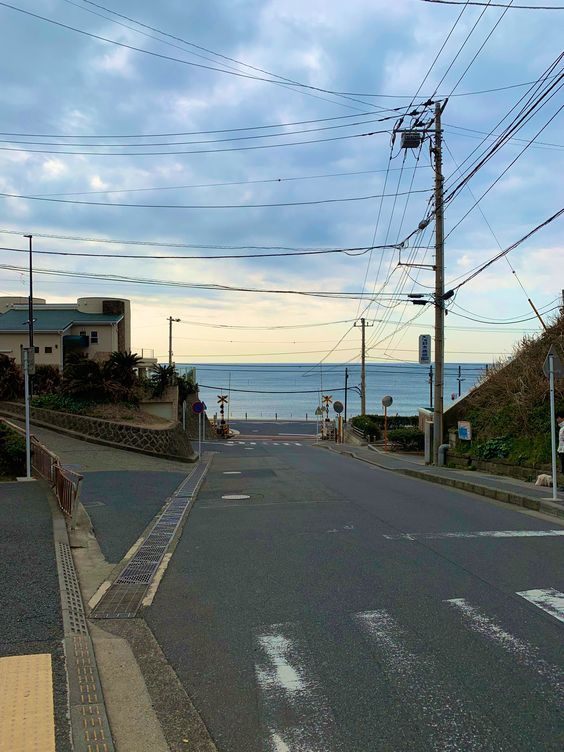 an empty street next to the ocean with power lines in the air and telephone poles above