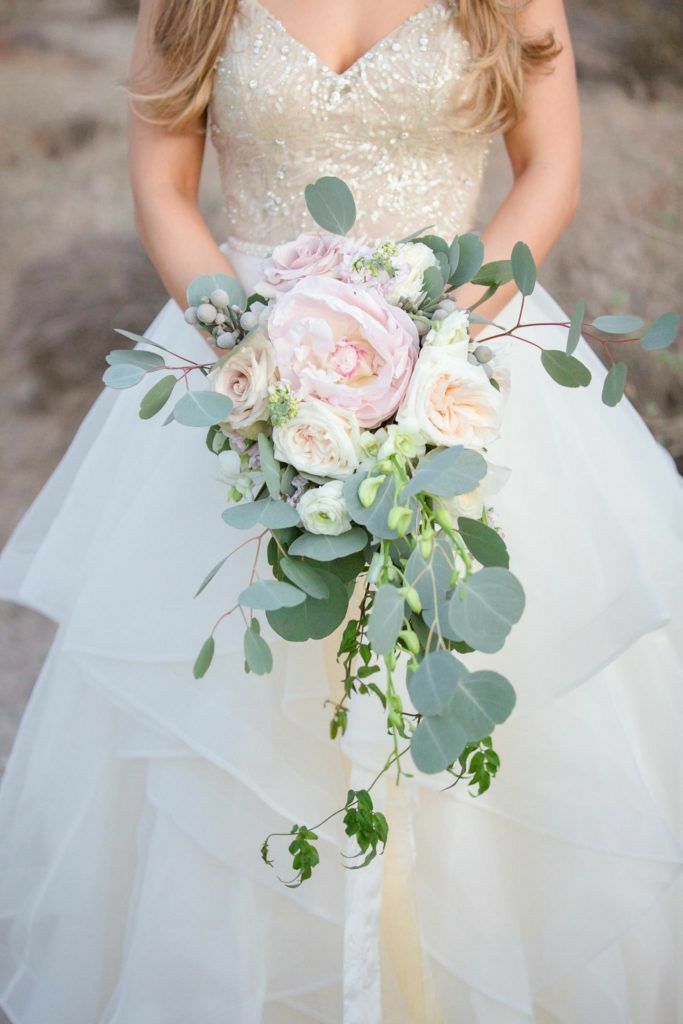 a woman in a wedding dress holding a bridal bouquet with greenery and flowers