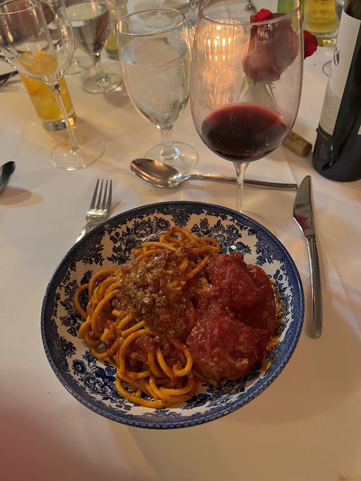 a plate of spaghetti and meatballs on a table with glasses of wine in the background