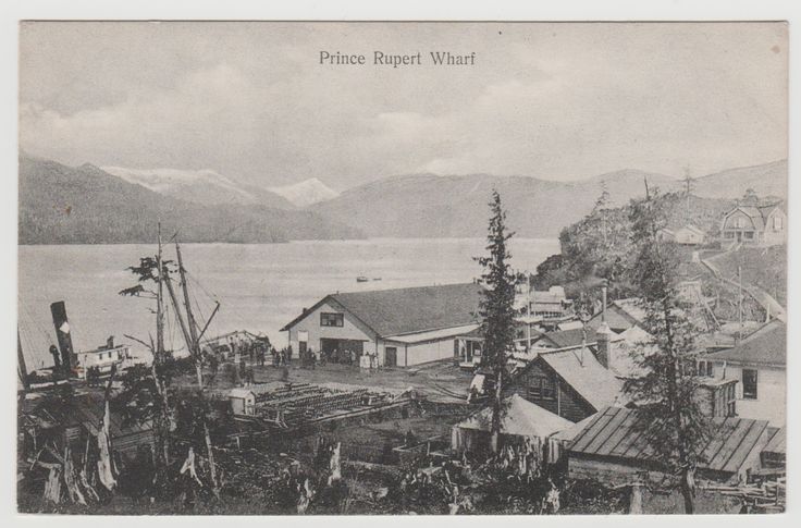 an old black and white photo of a town by the water with mountains in the background