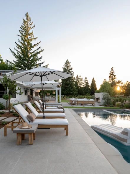 an outdoor pool with lounge chairs and umbrellas next to the swimming pool at sunset