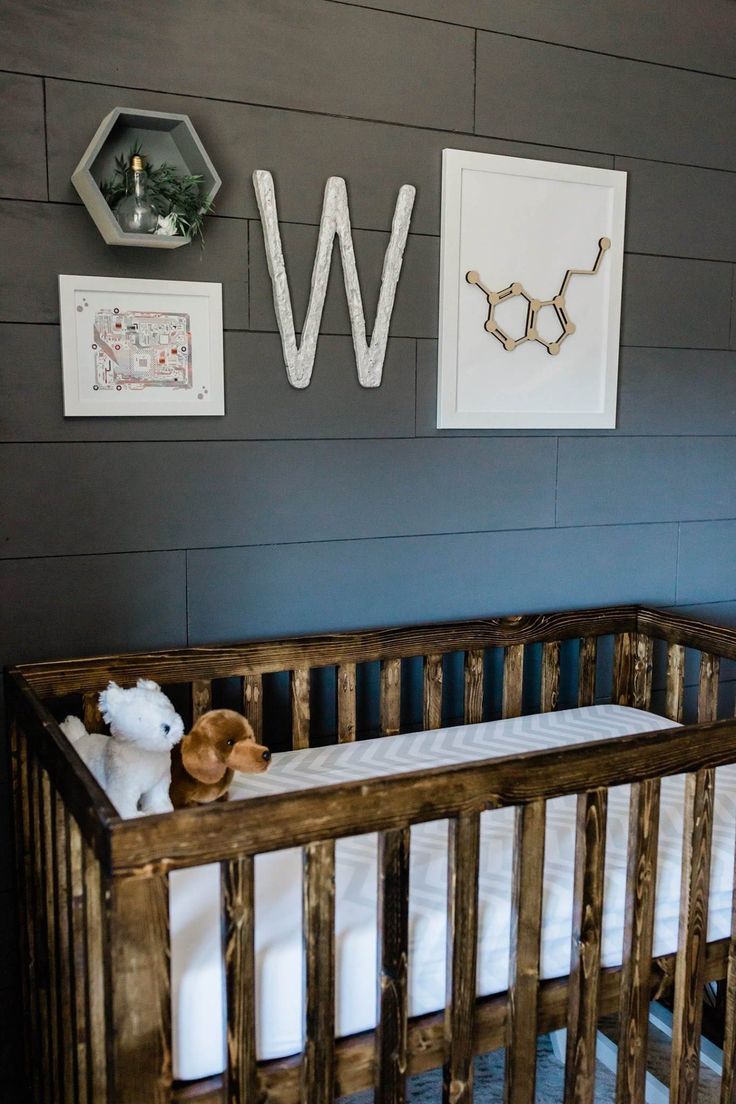 a wooden crib with two stuffed animals in it and the letter w on the wall