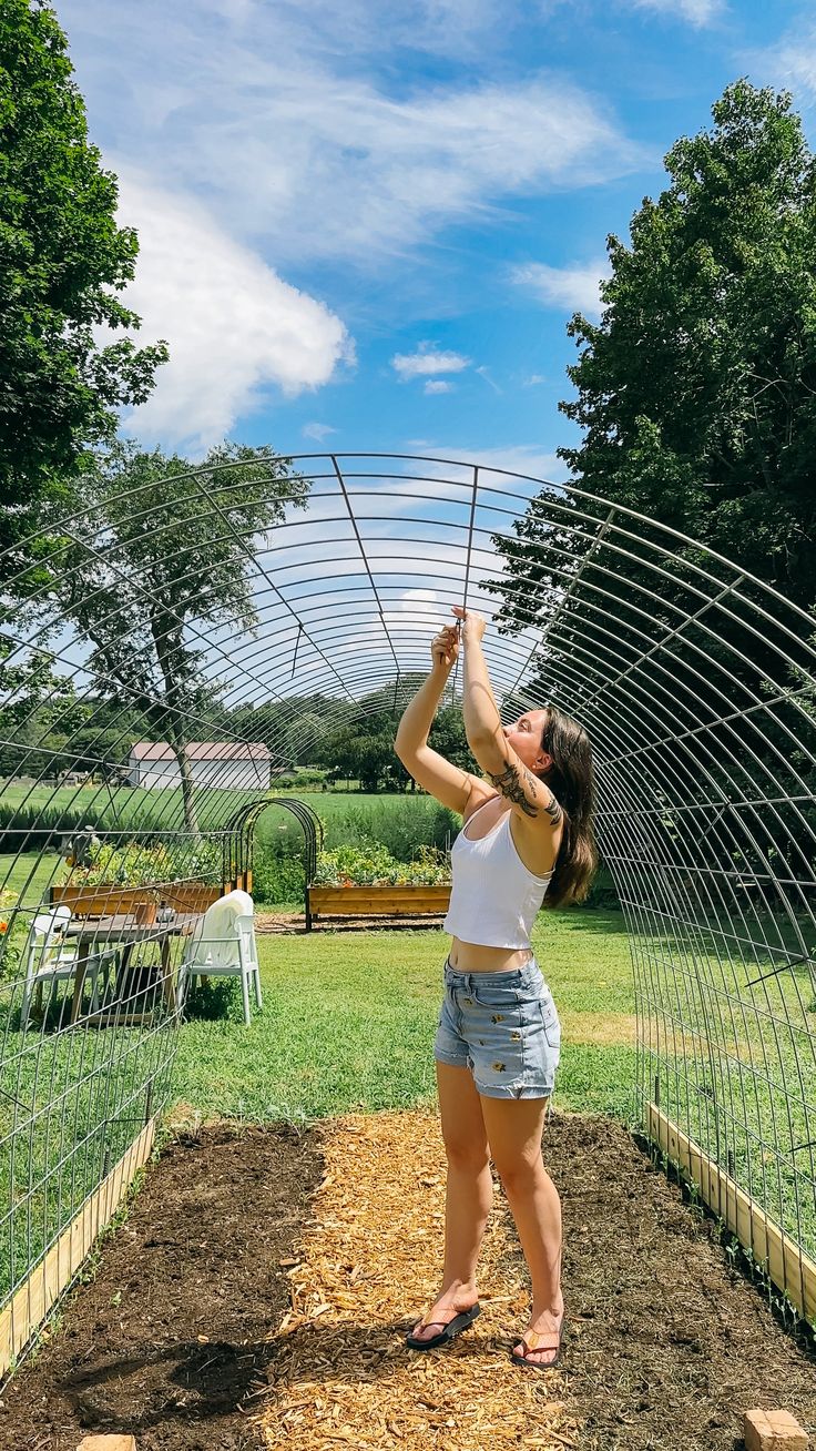 a woman is in the middle of an outdoor garden holding up a wire structure over her head