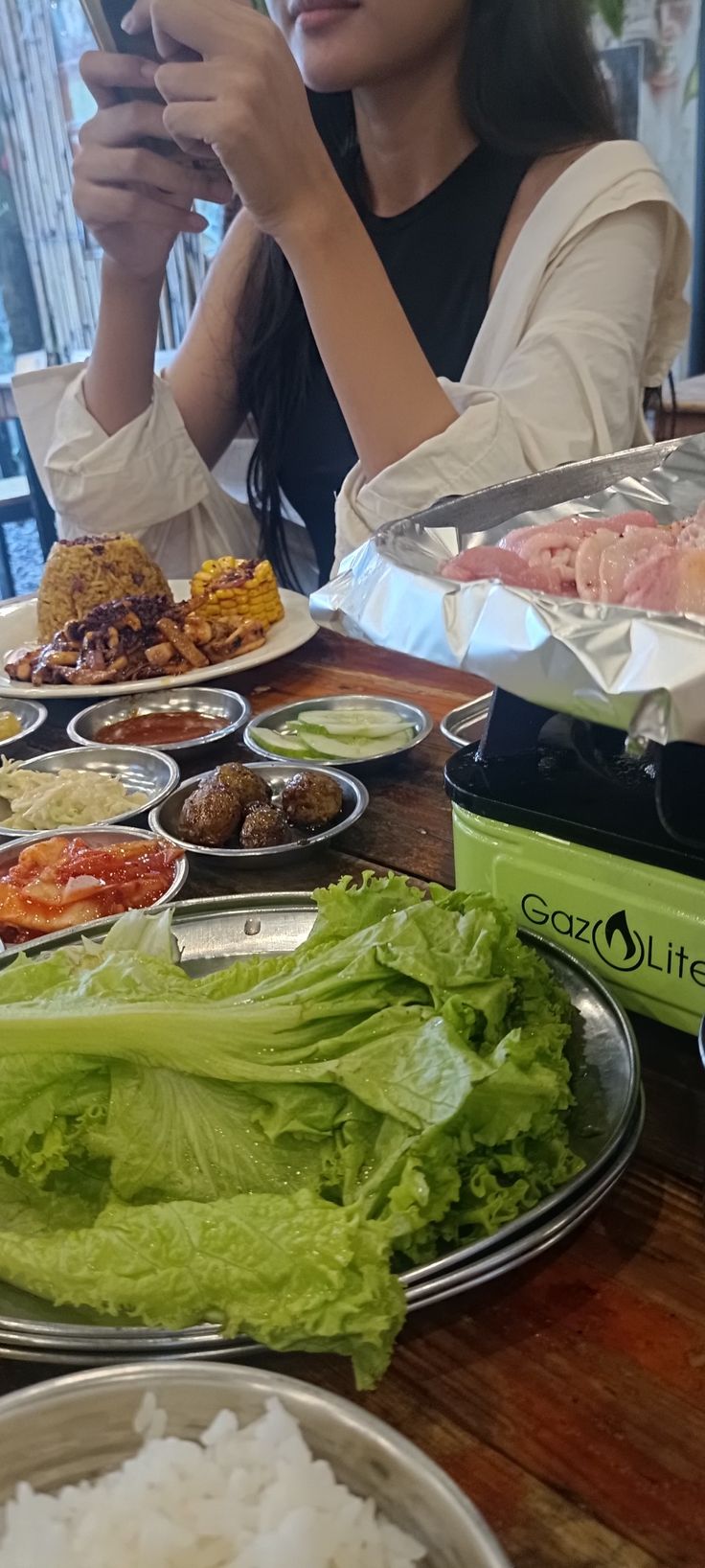 a woman is looking at her cell phone while sitting at a table full of food