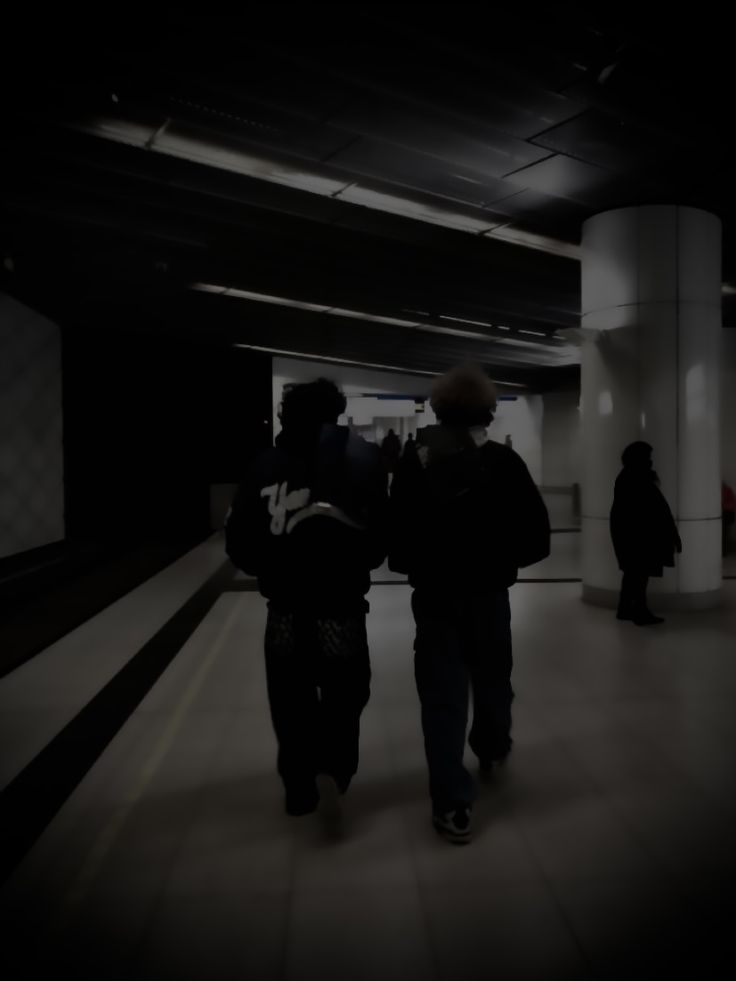 two people are walking through an empty subway station in the dark with their backs to each other