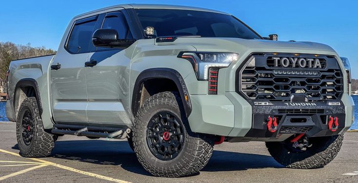 the front end of a gray truck parked in a parking lot next to some water