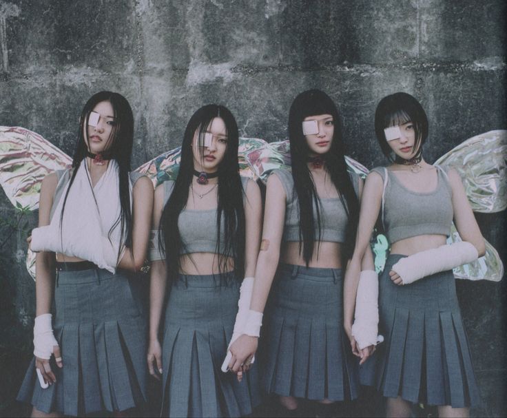 four girls with wings standing in front of a concrete wall and holding their arms around each other