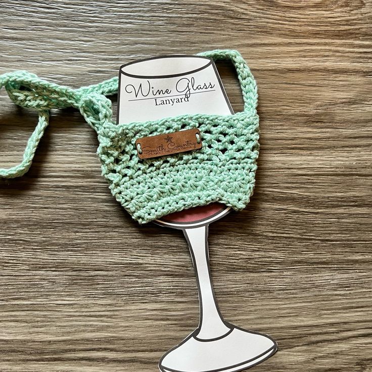 a crocheted wine glass with a label on it sitting on top of a wooden table