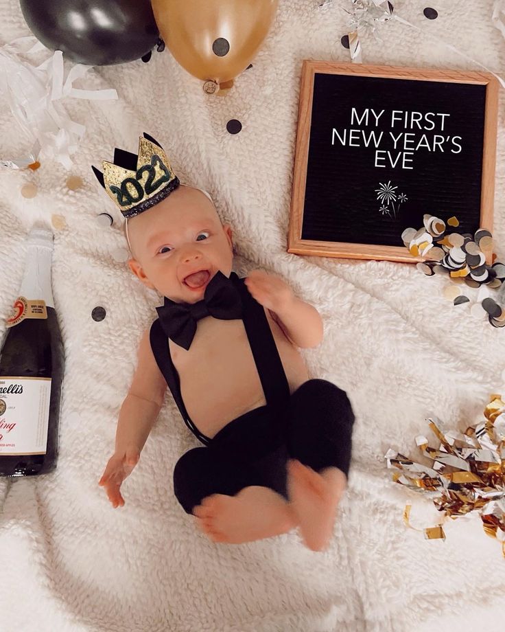 a baby wearing a black bow tie laying on top of a blanket next to balloons