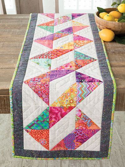 a table runner made with colorful quilts on top of a wooden table next to lemons