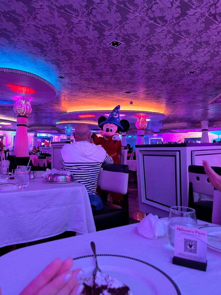 a person sitting at a table with a plate of food in front of them and mickey mouse on the ceiling