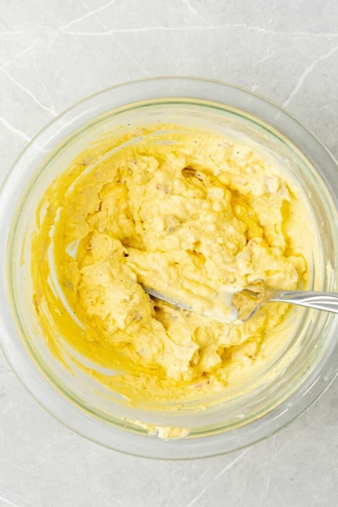 a glass bowl filled with yellow batter on top of a white countertop next to a silver spoon