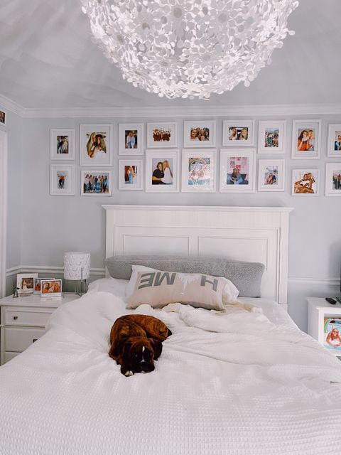 a dog laying on top of a white bed in a room with pictures on the wall