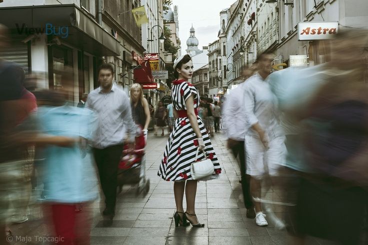 a woman in a striped dress is walking down the street while people walk by onlookers