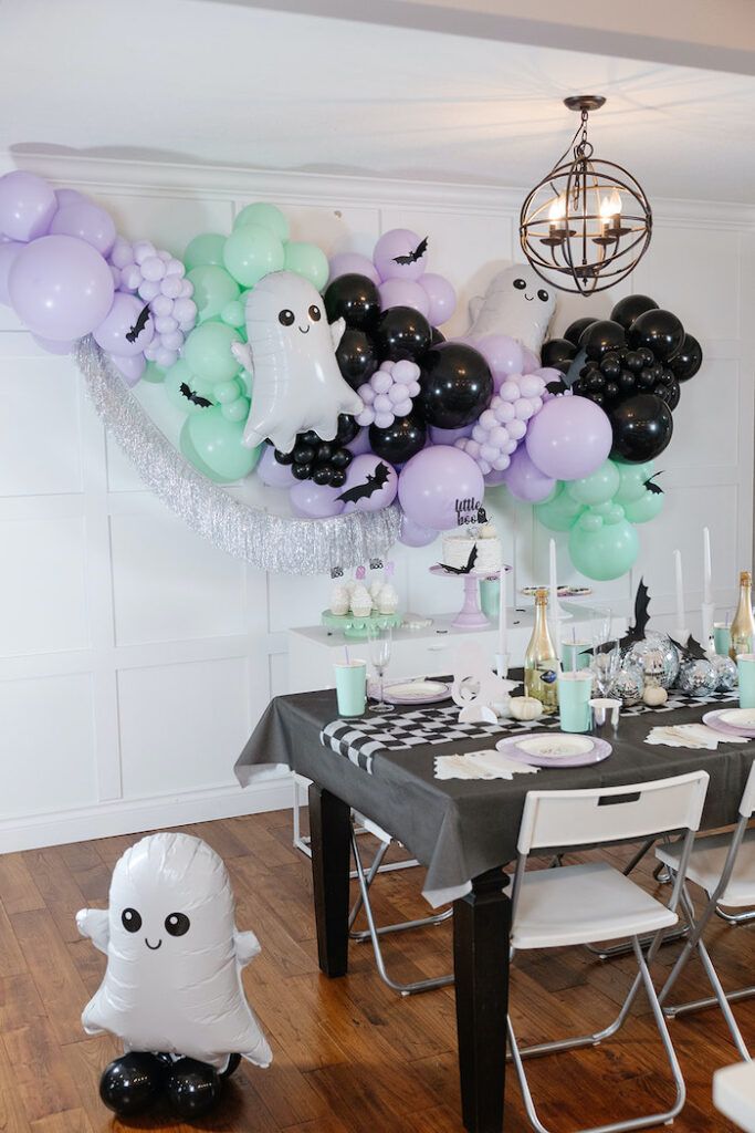 a dining room table with balloons and ghost decorations on the wall, along with an assortment of wine bottles