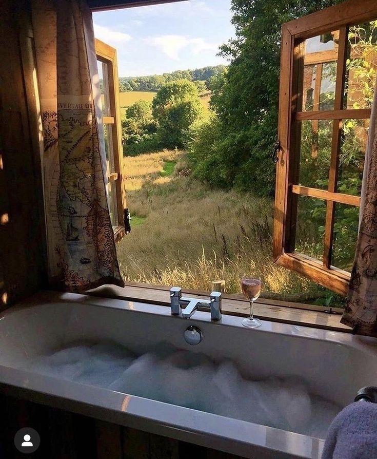 a bath tub sitting next to a window with an open view of a field outside