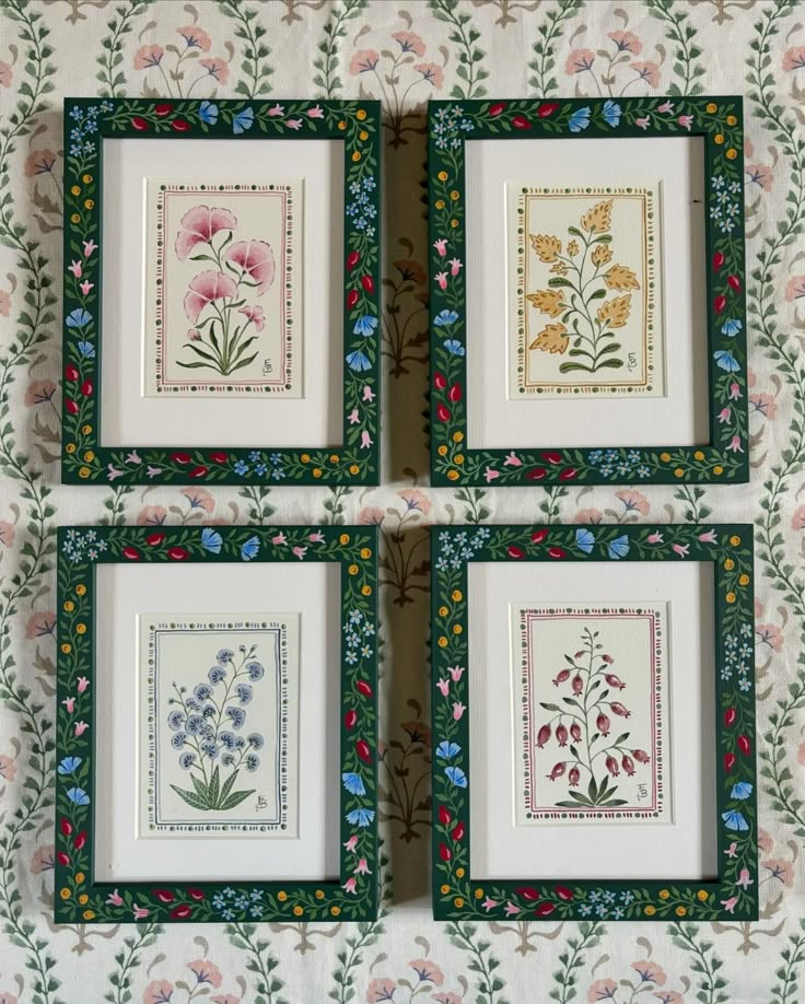 four framed pictures with flowers in them on a floral wallpapered tablecloth background