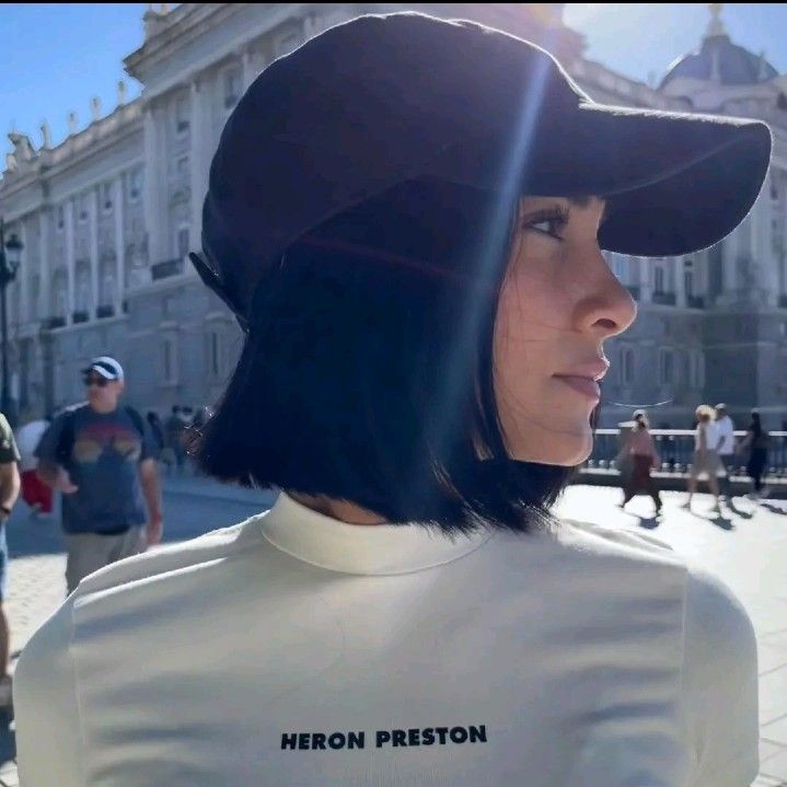 a woman wearing a white shirt and black hat with the words heron preston on it