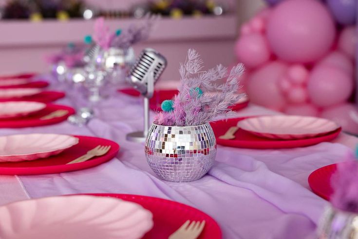 the table is set with pink and purple plates, silverware, and microphones