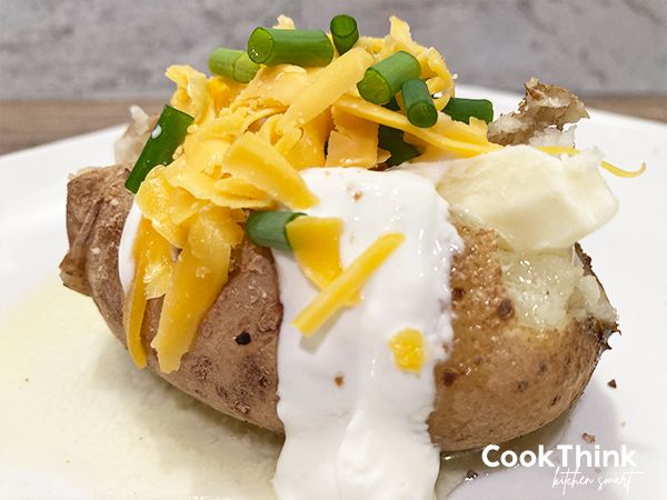 a baked potato with cheese and green onions on it sitting on a white plate next to a fork