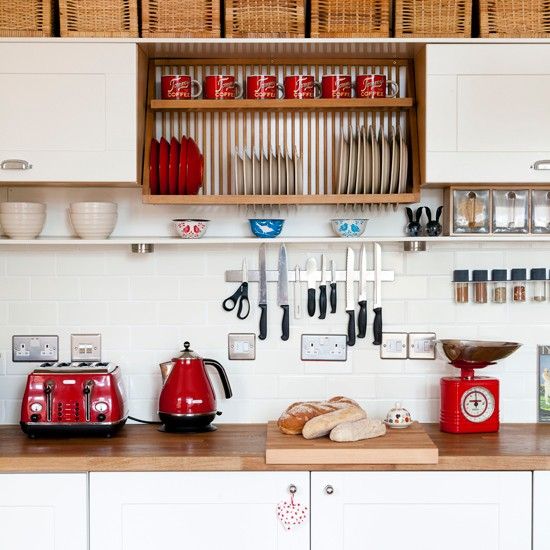 an organized kitchen with white cabinets and red appliances on the countertop, along with brown wicker storage bins