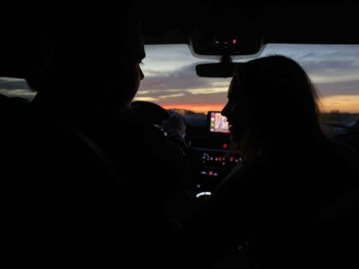 two people sitting in the back seat of a car at night, one person is driving