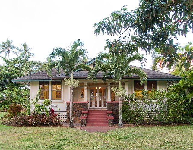 a small white house sitting in the middle of a lush green yard with palm trees