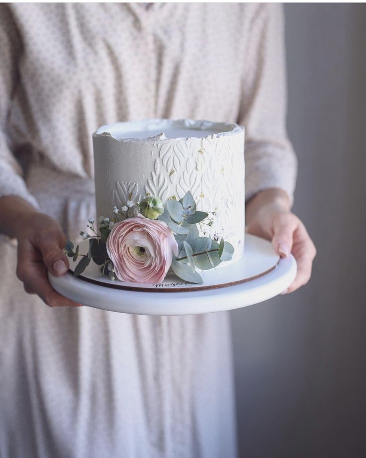 a woman holding a white cake with pink flowers on it