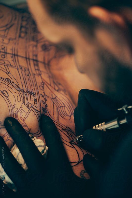 a man with tattoos on his chest holding a pen by an inking machine and looking down at the ground