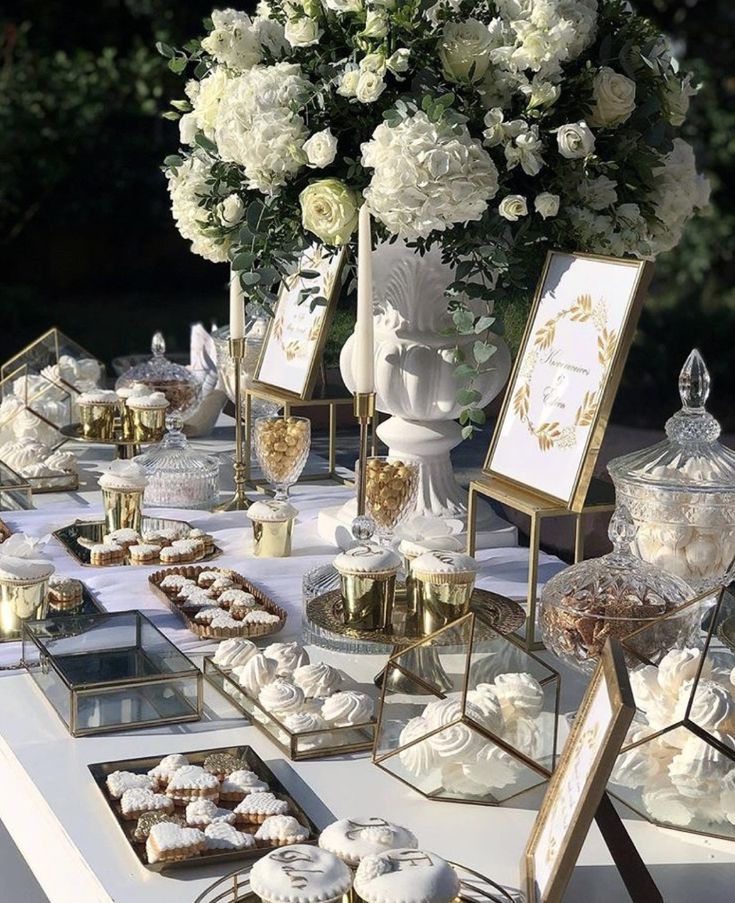 a table topped with lots of desserts next to a vase filled with white flowers