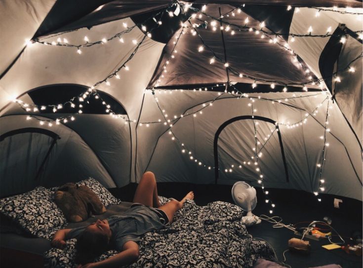 a person laying in a bed inside of a tent with lights strung from the ceiling