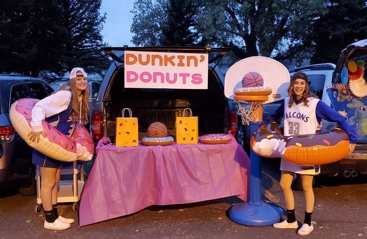 three women dressed in costumes standing next to a table with donuts on it and balloons