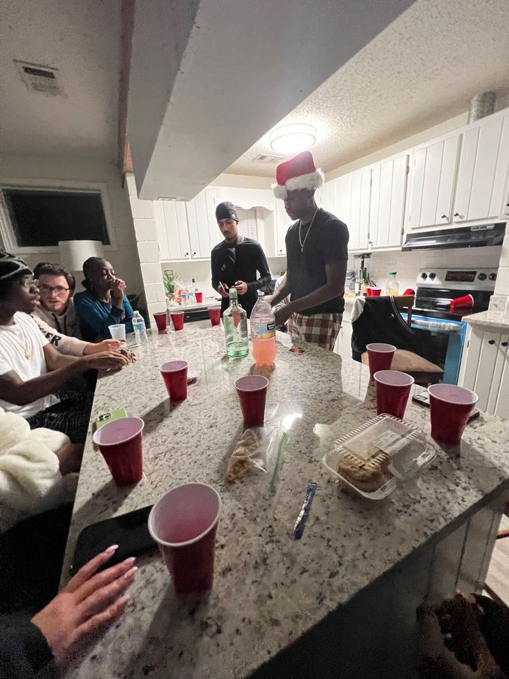 several people sitting at a kitchen counter with cups on it and one person standing in front of them