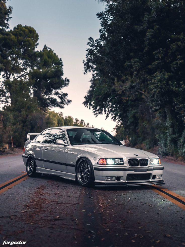 a silver car parked on the side of a road next to some trees and bushes