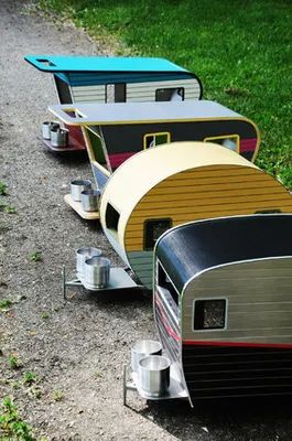 three toy trailers are lined up on the ground in front of some grass and trees