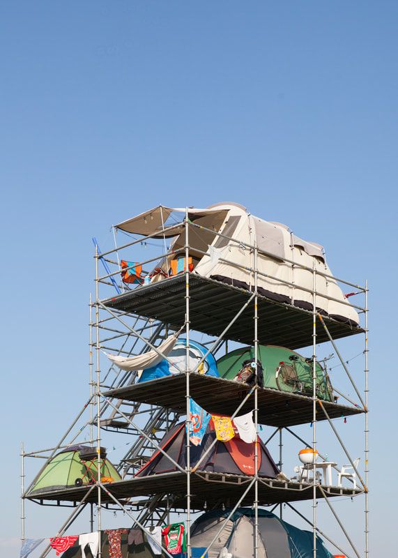 several people are sitting on scaffolding in front of tents