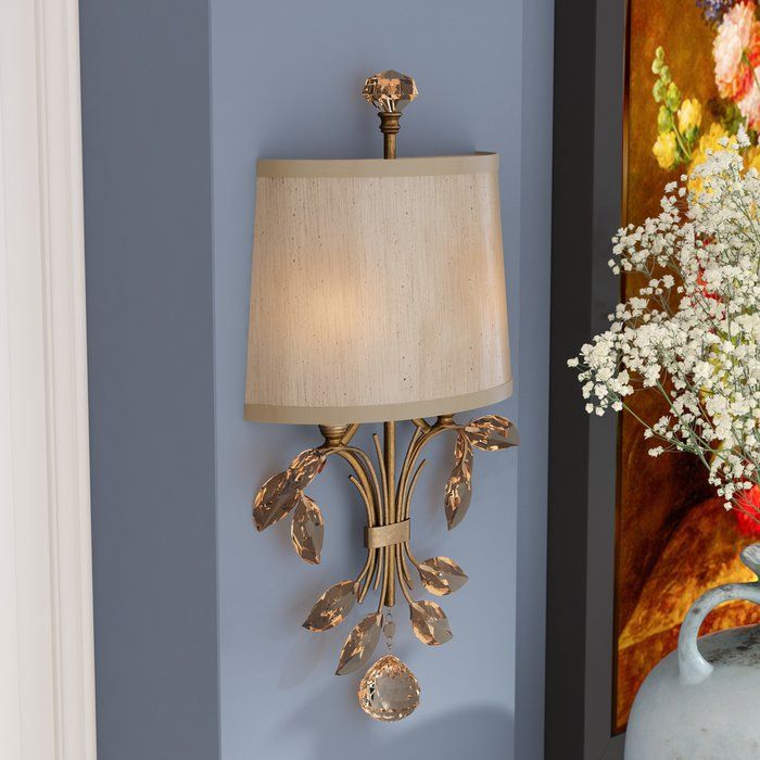 a lamp on the wall next to a vase with flowers and a painting behind it