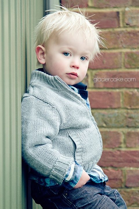 a young boy leaning against a brick wall