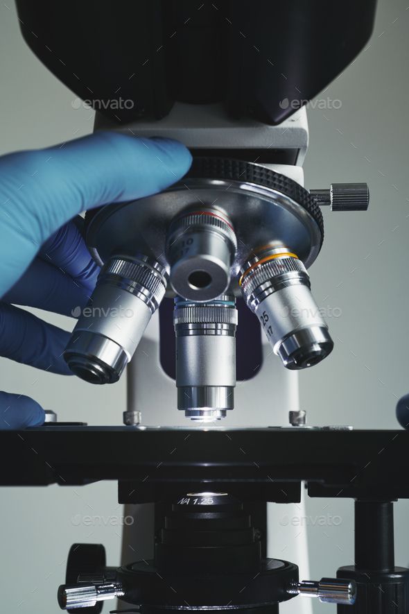 a person in blue gloves is looking through a microscope with their hands on the lens