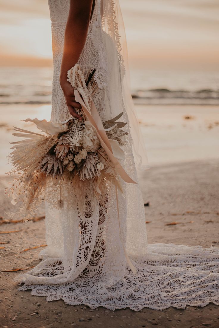 the bride is holding her bouquet on the beach