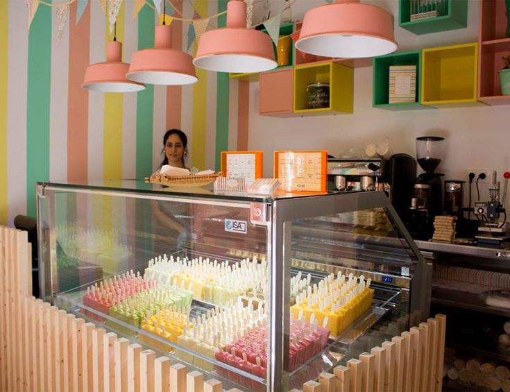 a woman standing behind a display case in a store filled with cakes and cupcakes