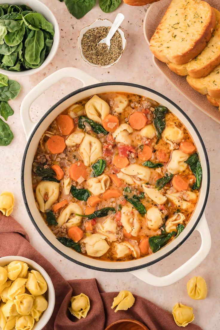 pasta and spinach soup in a white bowl surrounded by bread