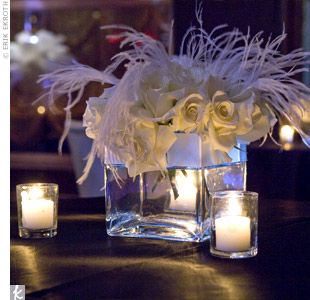 white flowers and candles are in a square glass vase on a black table with lights