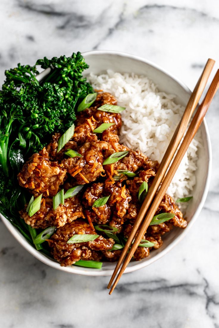 a bowl filled with meat and vegetables next to chopsticks on top of rice